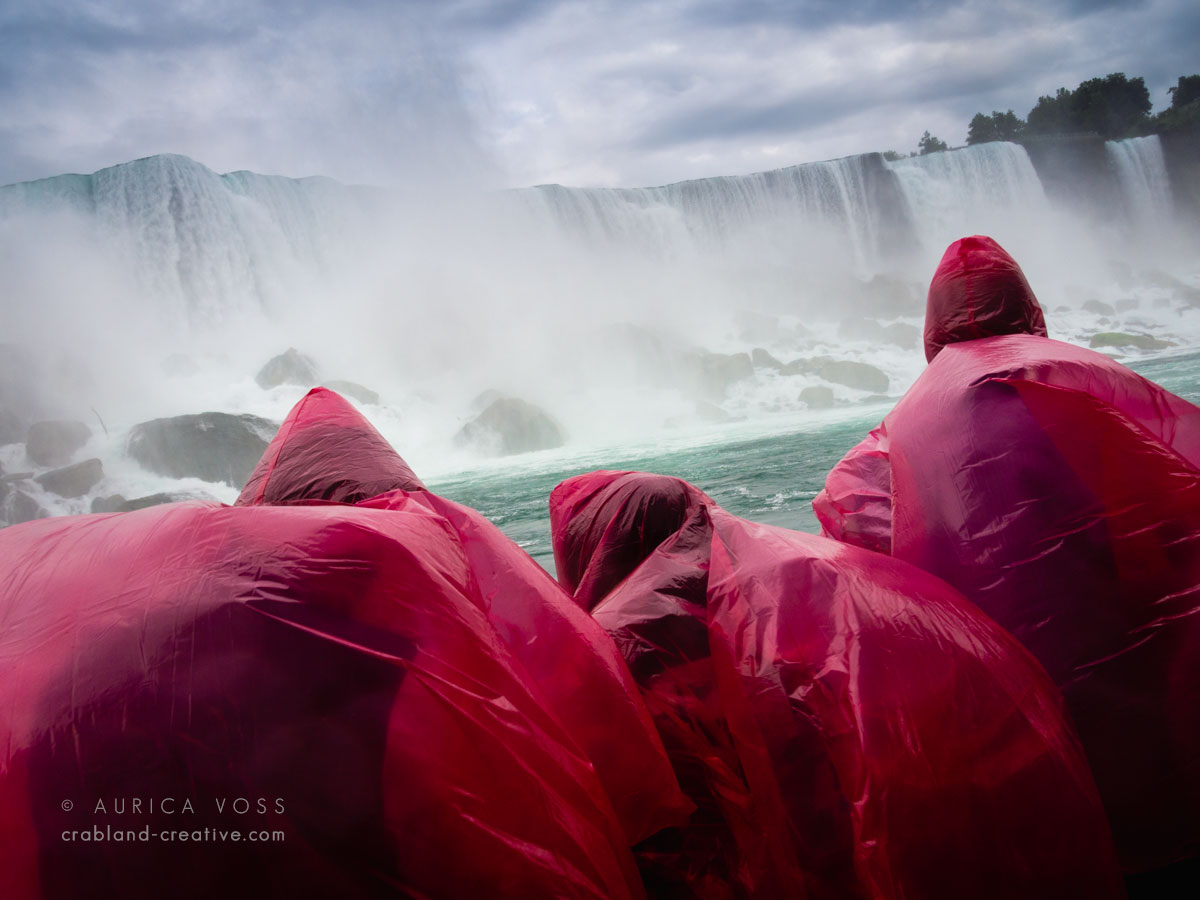 Drei Personen in pinken Regenponchos auf dem Ausflugsboot vor den Niagarafällen